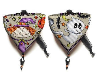 May include: Two reversible Halloween-themed dog bandanas with black and orange trim. One side features a cartoon witch with a purple hat and orange hair. The other side features a white ghost with black eyes and a black mouth. Both bandanas have a black tassel.