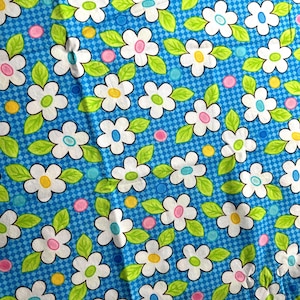 Peut inclure: Un tissu bleu avec un motif de marguerites blanches. Les marguerites ont des centres jaunes, roses et bleus. Le tissu a un motif à carreaux.