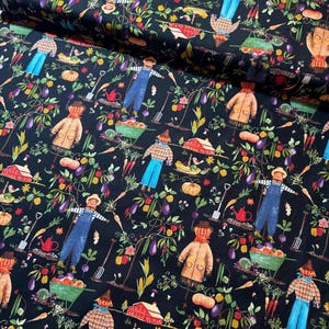 Op de afbeelding: Zwarte stof met een herhalend patroon van vogelverschrikkers, groenten en tuingereedschap. De vogelverschrikkers dragen overalls, jassen en hoeden. Pompoenen, wortelen en aubergines zijn verspreid over het ontwerp. Een rode schuur en kruiwagens zijn ook te zien.