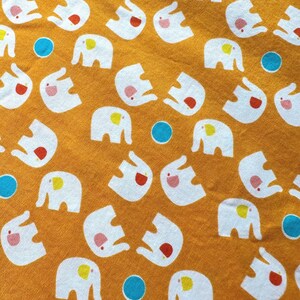 May include: A yellow fabric with a repeating pattern of white elephants with colourful accents. The elephants are all facing the same direction and have a playful expression.