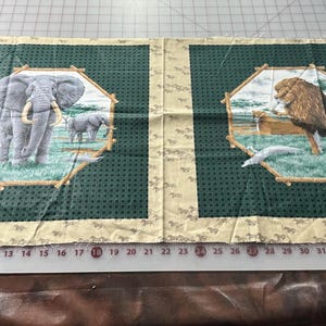May include: Two fabric panels with a green background and a beige border. Each panel features a different animal in a circular frame. The left panel shows an elephant with a brown trunk and tusks. The right panel shows a lion with a brown mane and a long tail.