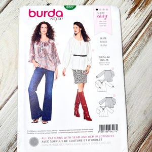 May include: A Burda Style sewing pattern packet, featuring a blouse design. The packet displays images of the finished blouses and includes sizing information for US sizes 8-18. The packet has the text "super easy" and "ALL PATTERNS WITH SEAM AND HEM ALLOWANCES".