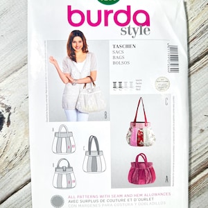 以下が含まれることがあります： 白いBurda Styleのパターンパッケージ。ハンドバッグのイラストが描かれています。パッケージには「TASCHEN, SACS, BAGS, BOLSOS」というテキストと「7264」の数字が含まれています。また、女性がハンドバッグを持っている様子も描かれています。