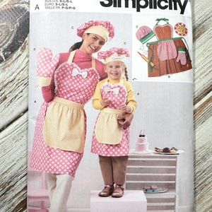 May include: Simplicity sewing pattern S3050 for matching aprons, oven mitts, and chef hats. The aprons are pink with white polka dots and yellow gingham pockets. The pattern includes sizes S-L.
