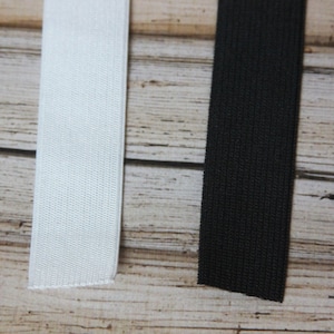 May include: Two pieces of elastic, one white and one black, are laid out on a wooden surface.