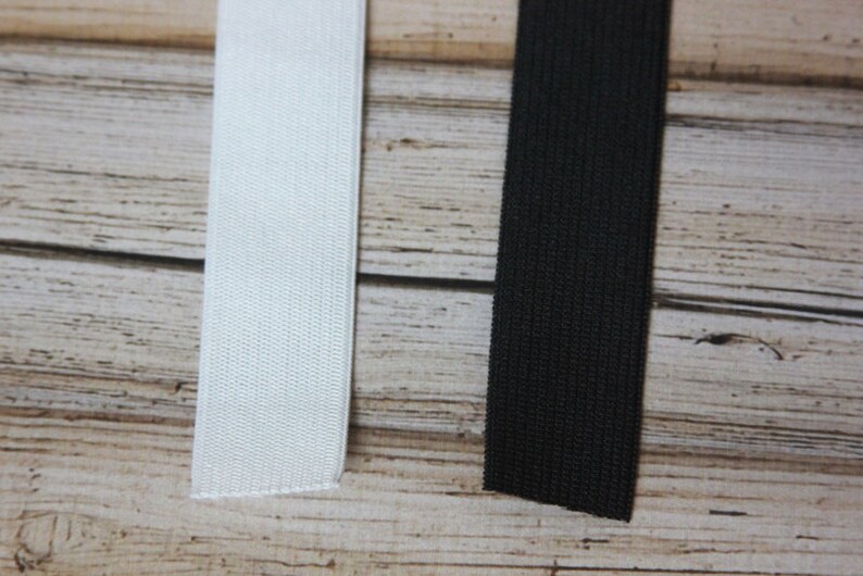 May include: Two pieces of elastic, one white and one black, are laid out on a wooden surface.