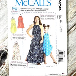 Op de afbeelding: McCall's naaipatroon M7589 voor beginner jurken. Het patroon bevat instructies en illustraties voor verschillende jurkstijlen, waaronder een halterjurk en een maxi-jurk. De omslag toont afbeeldingen van de afgewerkte jurken en de tekst "Learn to Sew for Fun."