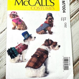 May include: McCall's Costumes pattern M7004 featuring four dogs in different outfits. The costumes include a plaid coat, a red and gray ensemble, a pink outfit, and a blue and burgundy outfit. The pattern is size OSZ.