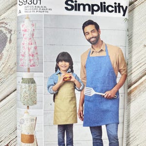 以下が含まれることがあります： SimplicityのソーイングパターンS9301、エプロンが特徴です。大人と子供向けのエプロンの画像が掲載されており、さまざまなスタイルがあります。表紙にはエプロンを着た男性と子供が写っています。パターンサイズはS-XLです。