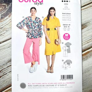 May include: A Burda Style sewing pattern packet featuring illustrations of a dress and blouse. The packet displays two women modeling the garments. The text on the packet includes "Kleid & Bluse" and "Dress & Blouse". The packet is white with pink and yellow accents.