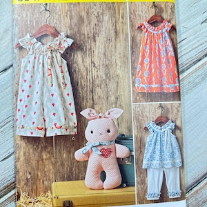 May include: Simplicity sewing pattern 8347 featuring children's clothing and a stuffed bunny. The pattern includes a dress, top, and pants, with sizes 1/2-4. The cover has a yellow header and the text "Ruby Jean's Closet".