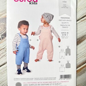 Pode incluir: Um padrão de costura para macacões infantis. A embalagem apresenta duas crianças usando macacões azuis e rosa. A marca "burda kids" está no topo, juntamente com o número do padrão 9295. O texto "PANTS WITH BRACES" também é visível.