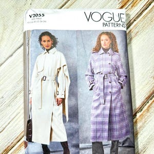 May include: Vogue Patterns sewing pattern featuring two trench coat designs. One coat is solid cream-colored, the other is a purple plaid. The pattern includes sizes 18-26. The package is white with the Vogue Patterns logo.