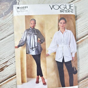 Peut inclure: Patron de couture Vogue Patterns R12221 avec deux modèles de chemisiers. L'un est argenté métallisé avec un nœud, l'autre est blanc avec une ceinture. Le patron comprend les tailles 36-44. Le logo Vogue Patterns est en haut.
