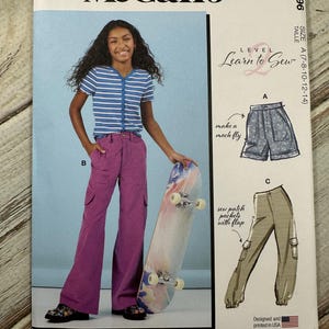 May include: McCall's sewing pattern featuring a young person wearing a striped shirt and purple pants. The pattern includes illustrations for shorts and pants with pockets. The text reads "Learn to Sew" and "Designed and printed in USA."