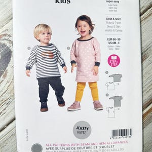 Può includere: Un modello di cucito Burda Kids per abbigliamento in jersey per bambini. Il modello include le istruzioni per un vestito e una maglietta. La copertina presenta due bambini che indossano i vestiti. Il modello è per le taglie EUR 68-98 e US 6M-3.