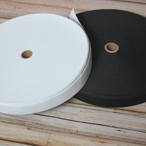 May include: Two spools of elastic, one white and one black, are rolled up on a wooden surface.
