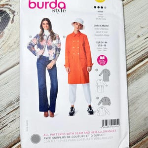 May include: A Burda Style sewing pattern packet featuring illustrations of a jacket and coat. The packet includes the text "Jacke & Mantel" and "Jacket & Coat". The pattern size range is EUR 34-44 and US 8-18. The packet is white with a colorful design.