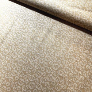 Puede incluir: Tela beige con un patrón repetido de contornos de calabazas blancas. Las calabazas son de diferentes tamaños y están distribuidas por la tela. La tela está doblada en la esquina superior izquierda.