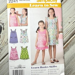 Pode incluir: Padrão Simplicity Learn to Sew, tamanho HH 3,4,5,6. A embalagem apresenta ilustrações de vestidos e o texto "Learn Basics Skills". Inclui instruções para escolher o tamanho certo, cortar um padrão, aplicar acabamentos e muito mais.