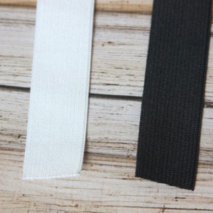 May include: Two pieces of elastic, one white and one black, are laid out on a wooden surface.