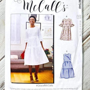 May include: A McCall's sewing pattern package featuring a white eyelet dress design. The package includes illustrations of different dress styles, with the text "McCall's" in elegant script. The hashtag #GraceMcCalls is also visible.