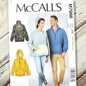 May include: A McCall's sewing pattern for jackets. The pattern features illustrations of different jacket styles, including a camouflage print jacket, a light blue hooded jacket, and a yellow hooded jacket. The pattern includes the text "McCall's" and the pattern number M7986.