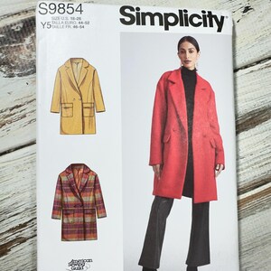 May include: Simplicity sewing pattern S9854. The pattern features illustrations of a double-breasted coat in yellow and plaid, and a photo of a woman wearing a red coat. The pattern size is U.S. 18-26.