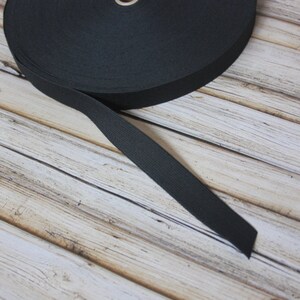 May include: A roll of black elastic band, approximately 2.5 cm wide, on a wooden surface.