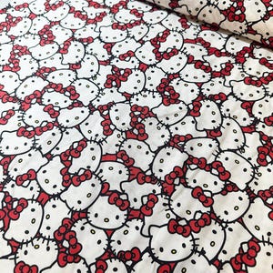 May include: White fabric with a repeating pattern of Hello Kitty faces. The faces are black and white with red bows.
