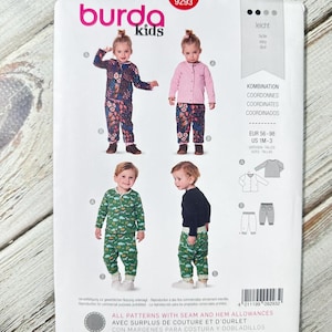 Puede incluir: Un patrón de costura para ropa de niños, con el logo "burda kids" y el número "9293". El paquete blanco presenta cuatro conjuntos diferentes: un conjunto floral, un conjunto de cárdigan rosa y un conjunto con estampado verde. Tallas EUR 56-98 y US 1M-3. El texto "CON MARGENES PARA COSTURA Y DOBLADILLOS" es visible.
