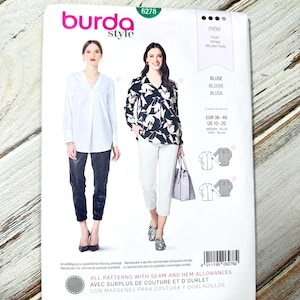 Puede incluir: Un patrón de costura Burda Style, número 6278, con dos mujeres modelando blusas. El paquete incluye la palabra "BLUSA" y otros textos en varios idiomas. El nivel de dificultad es "mittel".