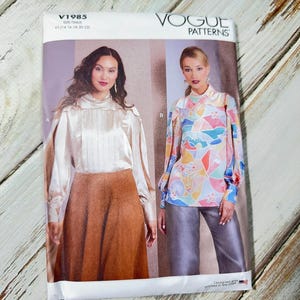 Peut inclure: Pochette de patron de couture Vogue Patterns avec deux modèles de chemisiers. L'enveloppe porte le texte "V1985" et "Vogue Patterns". Les modèles de chemisiers comprennent un chemisier en satin et un chemisier à imprimé abstrait coloré.
