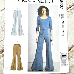 May include: A McCall's sewing pattern, M8007, featuring illustrations of flared pants and a photo of a woman wearing a denim jumpsuit. The pattern includes size A5 (6-8-10-12-14). The package is white with black text.
