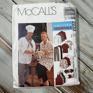 May include: A McCall's sewing pattern for Uniform Essentials, featuring images of chef attire. The pattern includes options for shirts, pants, aprons, and hats. The package shows a chef and a woman in a kitchen setting.