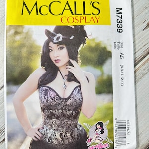 Peut inclure: Patron de couture McCall's Cosplay M7339. Le patron présente une femme dans un corset noir et argent et un chapeau à plumes. La taille du patron est A5 (6-8-10-12-14). La couverture a une bannière jaune avec le logo McCall's.