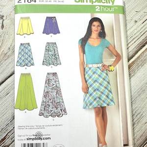 Puede incluir: Patrón de costura Simplicity 2184 con diseños de faldas. El patrón incluye varios estilos de faldas, con una modelo que lleva una falda a cuadros. El paquete incluye información de tallas y el logotipo de Simplicity.