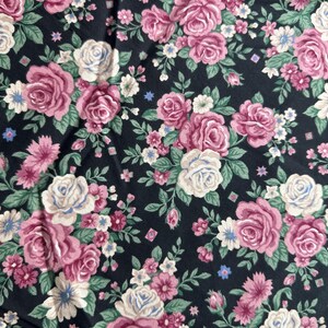 May include: Black fabric with a repeating pattern of pink, white and cream roses. The roses are surrounded by small green leaves and white flowers.