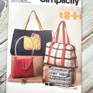 May include: Simplicity sewing pattern S3052 showing different bag designs. The image displays a tote bag, a red purse, a plaid handbag, and a small patterned bag. The pattern includes the text "easy-to-sew" and "Designed and printed in USA."