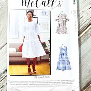 May include: A McCall's sewing pattern featuring a woman in a white eyelet dress. The pattern includes multiple view options with simple instructions. The pattern also shows illustrations of two other dress designs. The text "#GraceMcCalls" is visible.