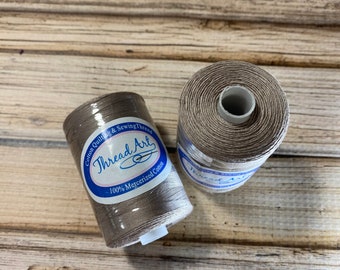 Puede incluir: Dos carretes de hilo de algodón marrón para acolchar y coser. Los carretes están etiquetados con "Thread Art" y "100% algodón mercerizado".
