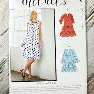 May include: McCall's sewing pattern M8090 featuring multiple dress designs. The pattern includes a model wearing a white dress with blue polka dots. The pattern also shows illustrations of a red dress and a blue dress. The text "#MarinaMcCalls" is visible.