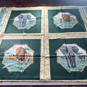 May include: A green and beige fabric with four octagonal panels featuring images of lions and elephants in a jungle setting. Each panel has a brown wooden frame.