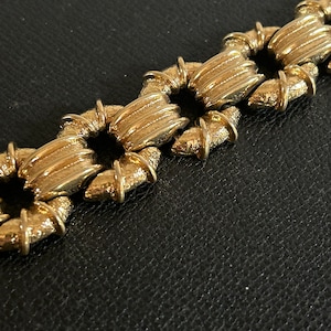 Peut inclure: Un bracelet chaîne en or avec un motif géométrique texturé. Chaque maillon est un carré aux bords arrondis et un motif en relief strié.