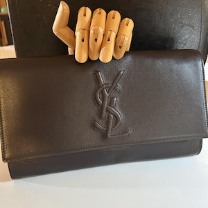 May include: A brown leather clutch with a large embossed YSL logo.