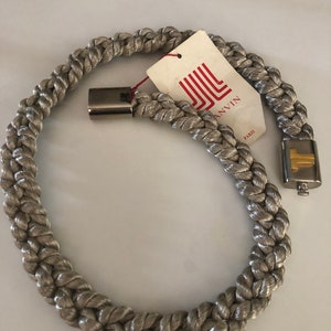 Puede incluir: Un collar de cuerda plateado con un cierre plateado y una etiqueta que dice "Jill Anvin Paris".