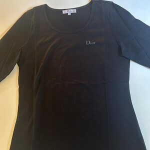 May include: Black long-sleeved shirt with a round neckline and the word "Dior" embroidered on the front.