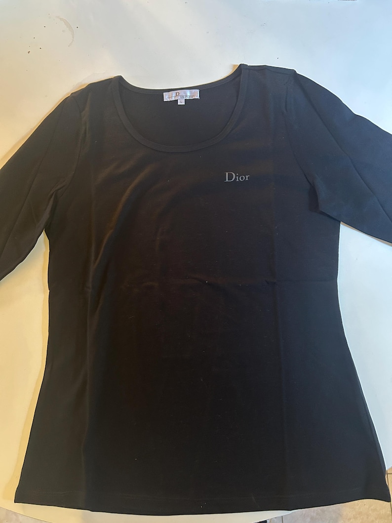 May include: Black long-sleeved shirt with a round neckline and the word "Dior" embroidered on the front.