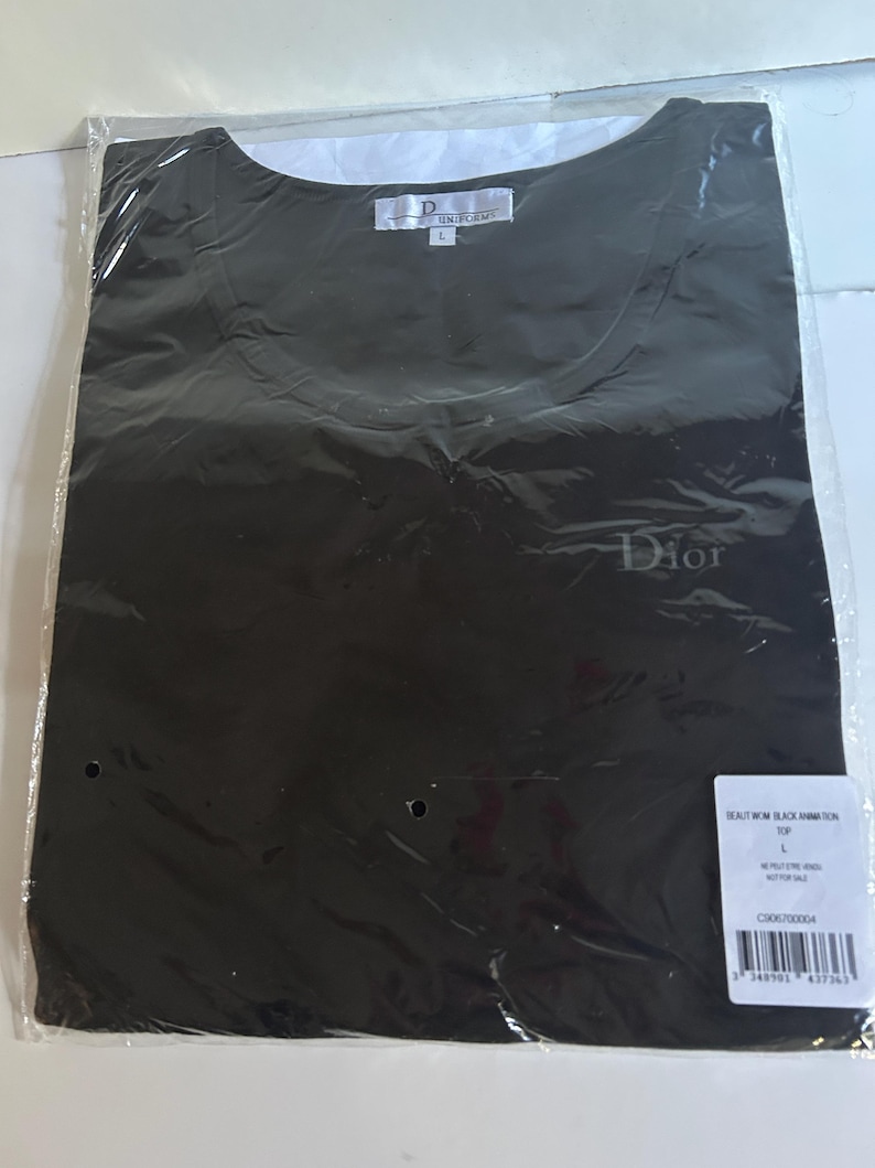 May include: Black t-shirt with a white Dior logo on the front. The shirt is packaged in a clear plastic bag with a white tag that reads "Beauty Worn Black Animation Top" and "Dior Homme".