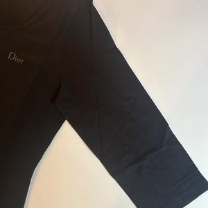 May include: Black long-sleeved t-shirt with a white "Dior" logo on the front.
